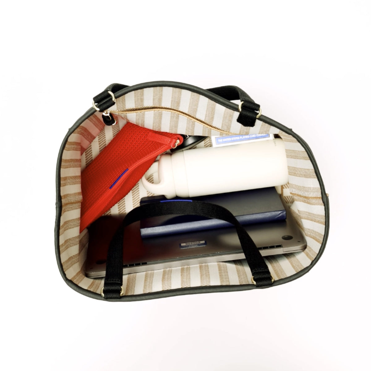 The Two-Way Tote in Sandbar is packed with a laptop, notebook, water bottle, a Petite Pouch and a deck of cards. In the interior pocket, small toiletries and a pair of sunglasses are added, and is then zipped closed. An iPhone is also zipped into the outer pocket. The model ties a scarf around the handle and carries the bag out of frame. 